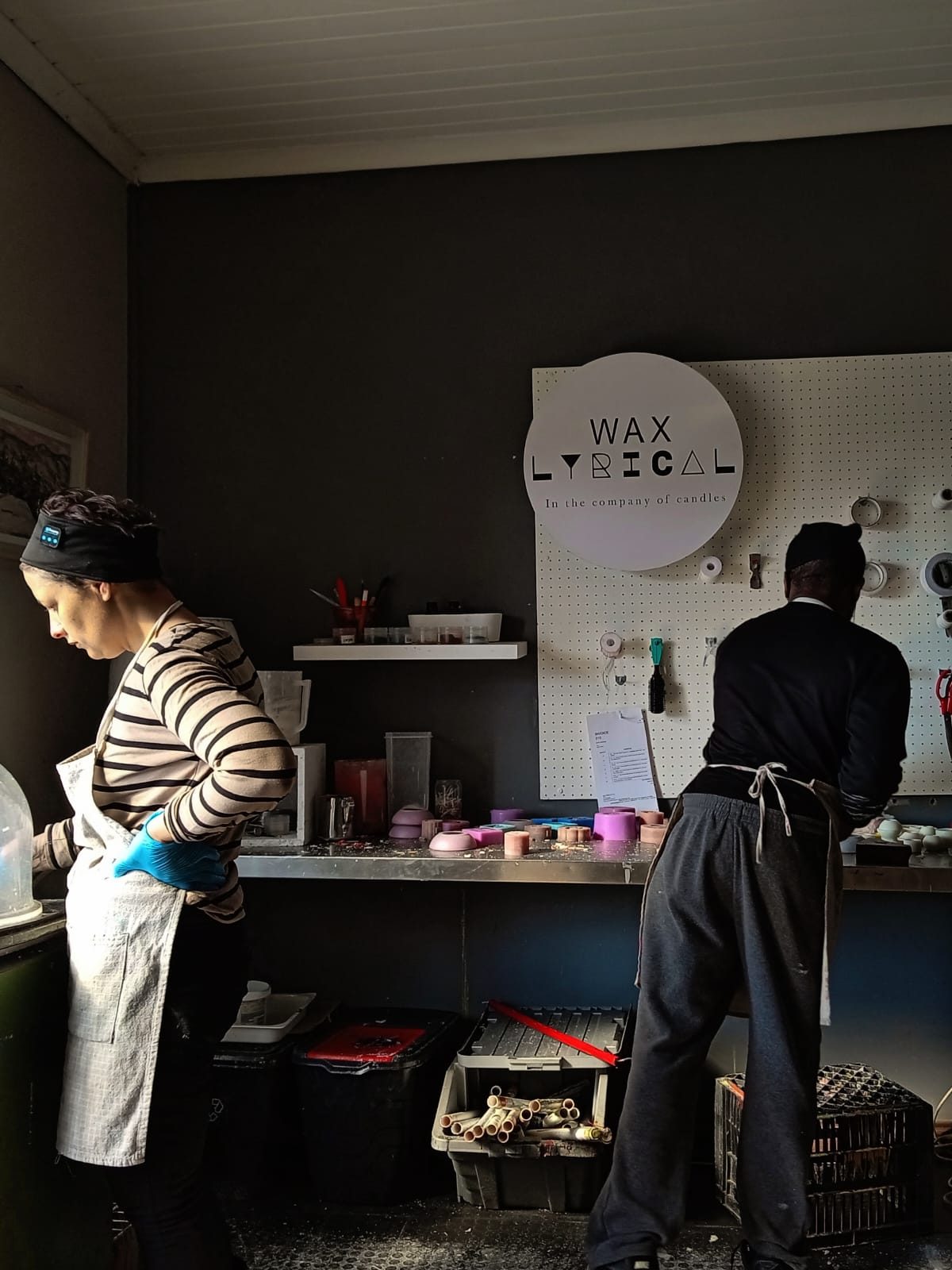 Two makers at work at the studio bench under the Wax Lyrical sign